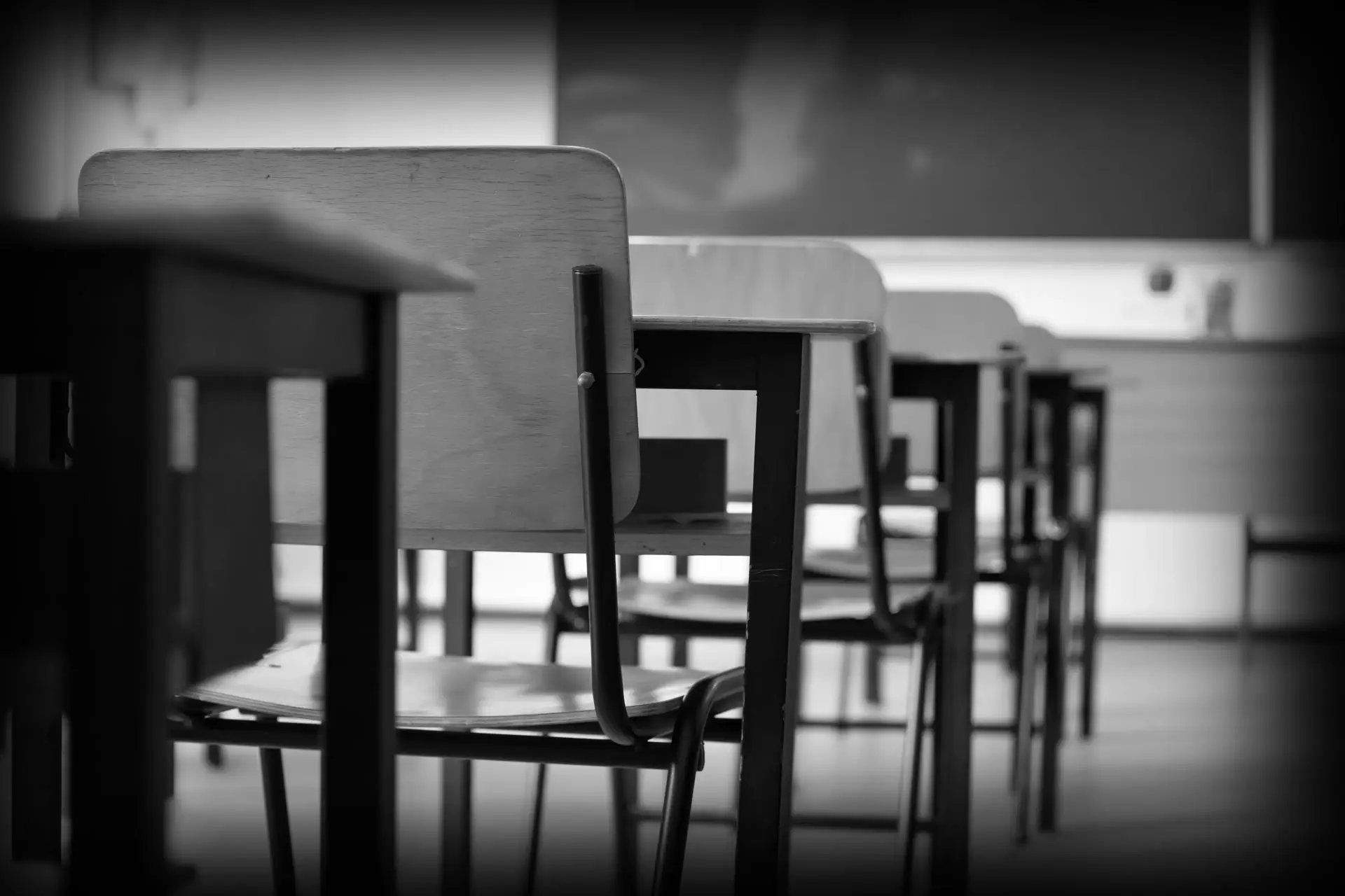 Row of empty desks in a quiet classroom, foreground desk in focus and others fading into the background.